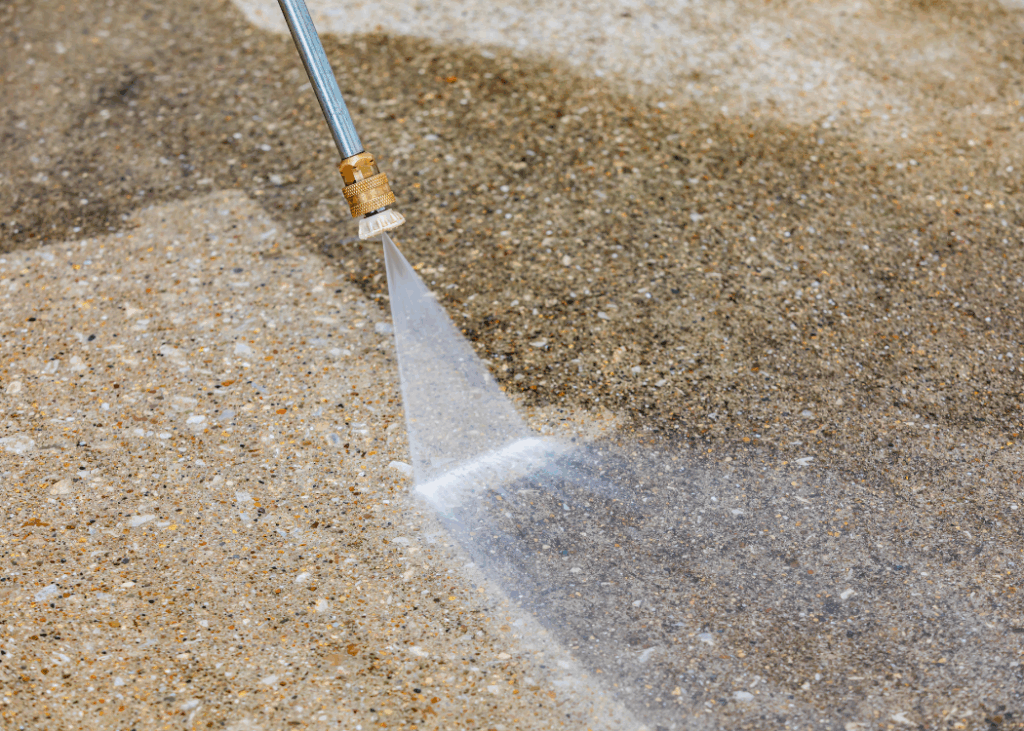 A person cleaning concrete with a hose, spraying water to remove dirt and debris from the surface.